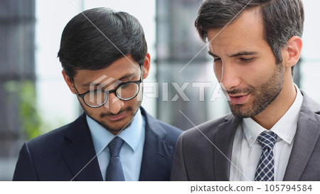 Business executive man and colleague standing in modern office hallway discussing project. 105794584