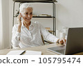 Smiling stylish mature woman sitting at desk with laptop and talking on mobile phone. 105795474