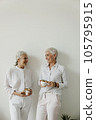 Senior females drinking coffee and laughing on white wall background. 105795915