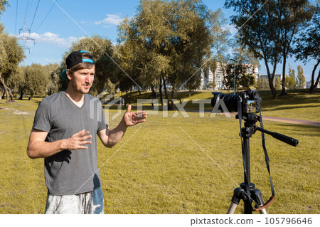 A young blogger records a video blog on a camera in the park. A young blogger records a video blog on a camera in the park. 105796646