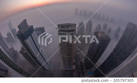 Rare early morning winter fog above the Dubai Marina skyline and skyscrapers lighted by street lights aerial night to day timelapse. Rare early morning winter fog above the Dubai Marina skyline and skyscrapers lighted by street lights aerial night to day timelapse. 105797305
