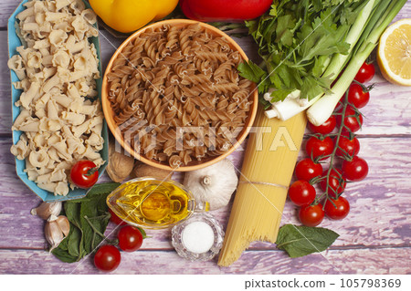 Italian pasta with vegetables, olive oil, spices on a wooden background,top view. Italian pasta with vegetables, olive oil, spices on a wooden background,top view. 105798369