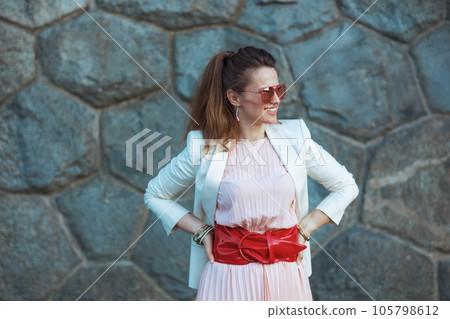 happy stylish woman in pink dress and white jacket in city 105798612