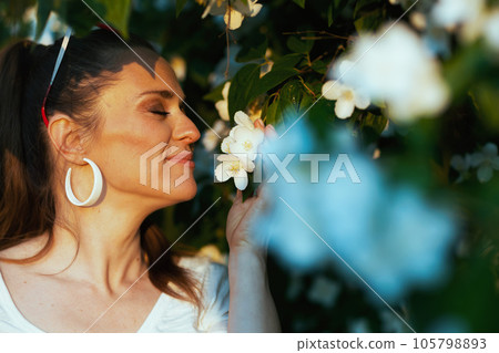 smiling stylish woman in white shirt near flowering tree smiling stylish woman in white shirt near flowering tree 105798893