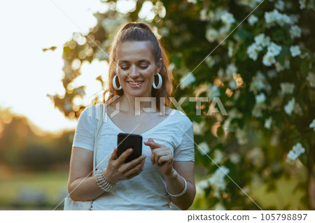 smiling trendy woman in white shirt using smartphone app 105798897