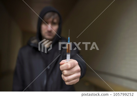 Addict holding a syringe in his hand on the street. 105799252
