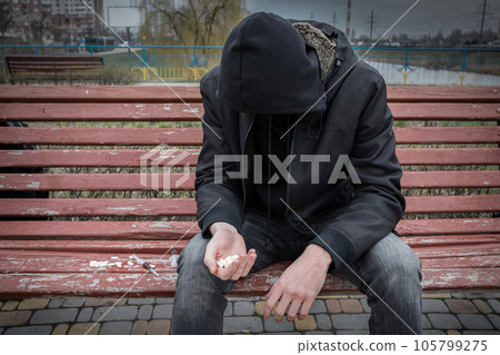 Homeless man addict and alcoholic sitting alone on a bench. Concept of drug addiction. Lifestyle 105799275