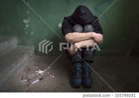 A young drug addict with folded arms in an abandoned house. A young drug addict with folded arms in an abandoned house. 105799281