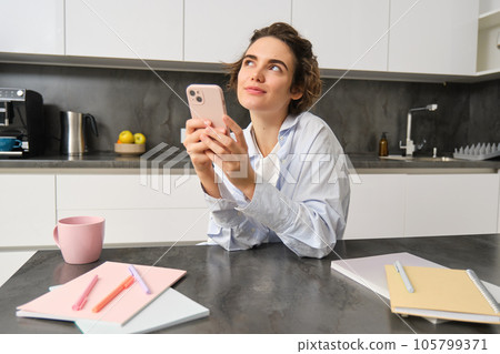 Candid smiling woman, holding smartphone in her kitchen, using mobile phone and looking happy 105799371