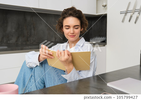 Portrait of modern girl, sits at home and reads through her notes, looks at journal, makes plans for week Portrait of modern girl, sits at home and reads through her notes, looks at journal, makes plans for week 105799427