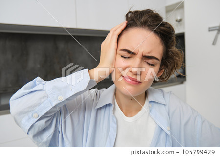 Close up portrait of brunette woman, touches her head, feels dizzy, has migraine or headache, grimaces from pain Close up portrait of brunette woman, touches her head, feels dizzy, has migraine or headache, grimaces from pain 105799429