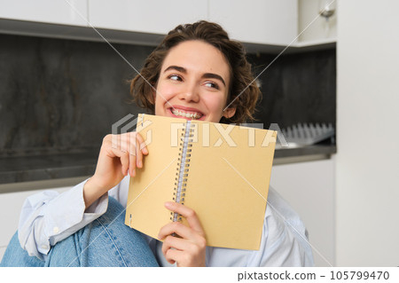 Happy young woman studying at home, reading journal, preparing for exam, looking at her notes in notebook Happy young woman studying at home, reading journal, preparing for exam, looking at her notes in notebook 105799470