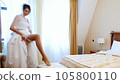 bride fees. beautiful, smiling bride, in veil and lace dress, puts on a lace garter on the leg, in a bright elegant bedroom. morning preparation wedding concept. 105800110