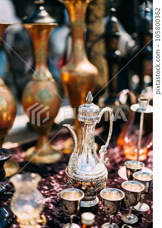 Oriental Style Ancient Jug At Flea Market. Metal Oriental Jug With Engraved Texture Floral Pattern. East Tableware. Old Tableware For Cofe And Tea Oriental Style Ancient Jug At Flea Market. Metal Oriental Jug With Engraved Texture Floral Pattern. East Tableware. Old Tableware For Cofe And Tea 105800362