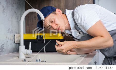 Male plumber tries to stop flow of water from faucet Male plumber tries to stop flow of water from faucet 105801438