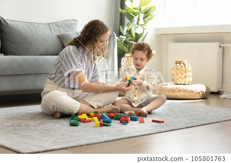 Positive caring young mom and cute kid playing toy blocks Positive caring young mom and cute kid playing toy blocks 105801763