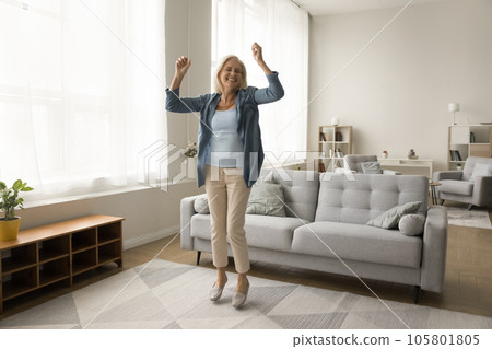 Cheerful excited older retired woman dancing in home living room Cheerful excited older retired woman dancing in home living room 105801805
