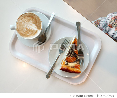 mug of cappucci with a pattern and a piece of cake on a white tray on a table 105802295