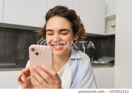 Portrait of beautiful woman at home, holding smartphone, online shopping from mobile phone app Portrait of beautiful woman at home, holding smartphone, online shopping from mobile phone app 105802412