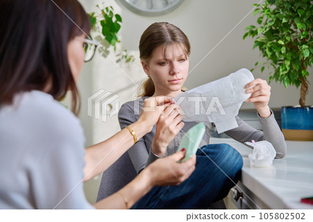Mother showing telling preteen daughter sanitary pads 105802502