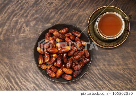 A plate with dates and a cup of tea on wooden background. Dried fruits. Ramadan concept. Arabic traditional food. Top view, flat lay. 105802850