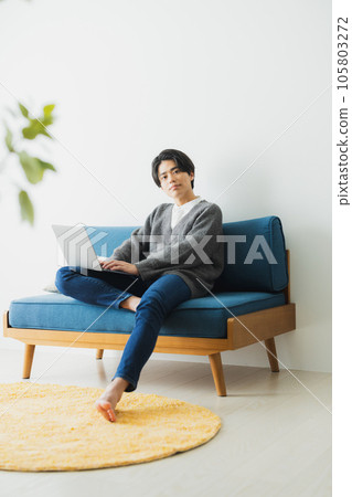 A young man sitting on the sofa in the living room and using a computer A young man sitting on the sofa in the living room and using a computer 105803272