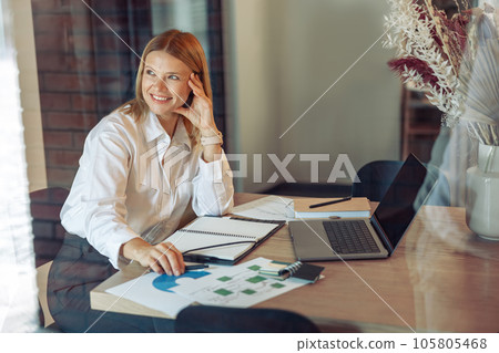 Woman analyst working with documents and use laptop while sitting in cozy coworking near window Woman analyst working with documents and use laptop while sitting in cozy coworking near window 105805468