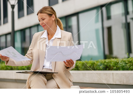 Stylish woman analyst working with documents while sitting outside on modern building background 105805493