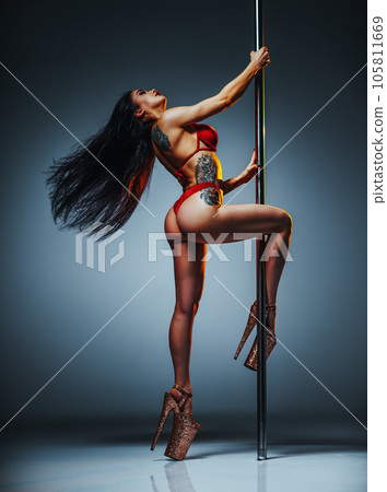 Young brunette woman pole dancing on gray wall background, tattoo on body 105811669