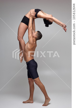 The couple of a young modern ballet dancers in black suits are posing over a gray studio background. The couple of a young modern ballet dancers in black suits are posing over a gray studio background. 105812644