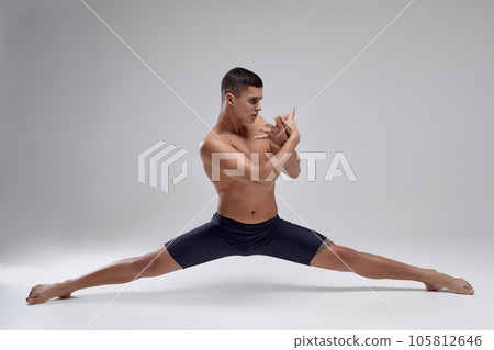 Photo of a handsome man ballet dancer, dressed in a black shorts, making a dance element against a gray background in studio. 105812646