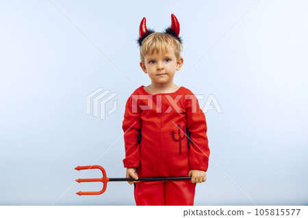 Happy cheerful boy in devil costume with trident on blue background Happy cheerful boy in devil costume with trident on blue background 105815577