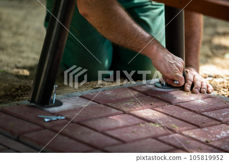 A construction worker bolts a park bench to paving stones. 105819952