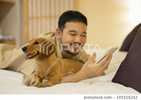 Man looking at his dog and smartphone on a hotel bed Man looking at his dog and smartphone on a hotel bed 105820282