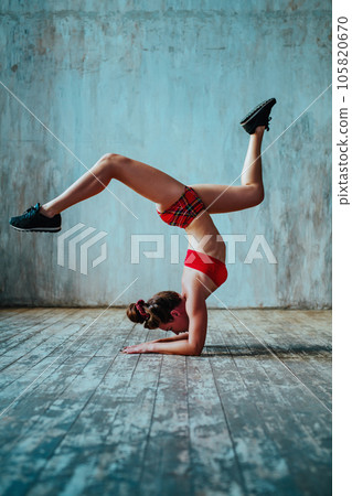 Young woman gymnast standing upside down on gray wall background Young woman gymnast standing upside down on gray wall background 105820670