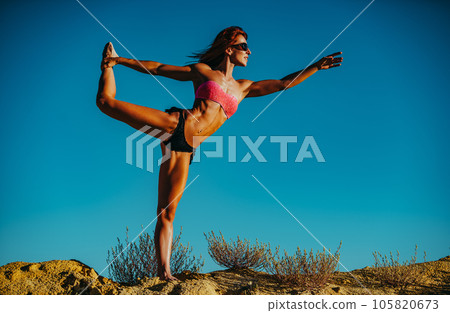 Sports woman standing at the top of the hill and looking aside on blue sky background Sports woman standing at the top of the hill and looking aside on blue sky background 105820673