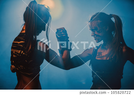 Two women fighters shaking hands in dark interior with smoke, tattoo on body 105820722
