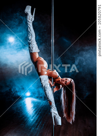 Young woman pole dancing on dark background with blue smoke Young woman pole dancing on dark background with blue smoke 105820791