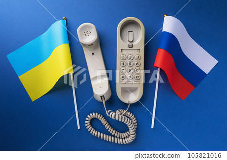 Old telephone and two flags on a blue background, a concept on the theme of telephone conversations between the Ukraine and Russia Old telephone and two flags on a blue background, a concept on the theme of telephone conversations between the Ukraine and Russia 105821016