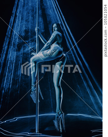 Young woman pole dancing in club with blue laser light, tattoo on body 105821054