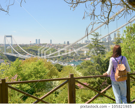 A young woman tourist with a backpack enjoys a panoramic view of the Fatih Sultan Mehmet Bridge. Back view. 105821985