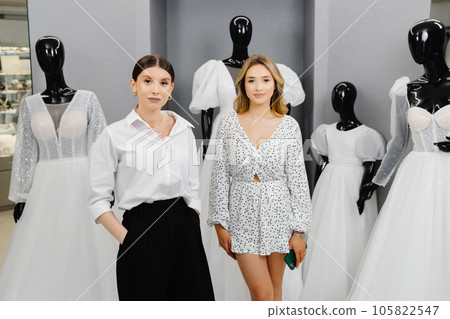 The bride-to-be came to a wedding dress salon to buy a dress. The assistant helps to choose a dress for the bride The bride-to-be came to a wedding dress salon to buy a dress. The assistant helps to choose a dress for the bride 105822547