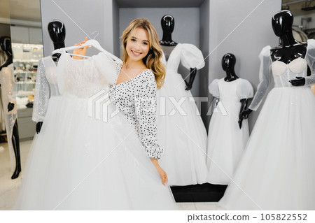 Young beautiful woman chooses a dress for wedding in a wedding salon Young beautiful woman chooses a dress for wedding in a wedding salon 105822552
