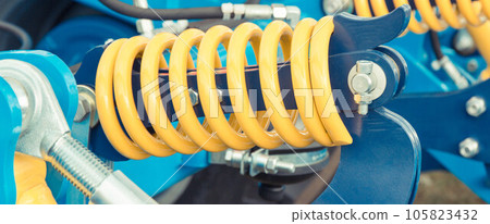 Hard spring made of steel. Part and detail of blue industrial or agricultural machine Hard spring made of steel. Part and detail of blue industrial or agricultural machine 105823432