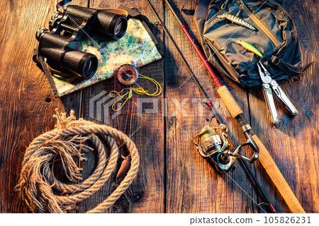 Fishing spinning with a reel line. Fishing items on a wooden background. Binoculars and rope. Copy space in centre. Fishing spinning with a reel line. Fishing items on a wooden background. Binoculars and rope. Copy space in centre. 105826231