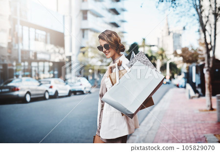 Shopping, spending and consumerism with a female shopper enjoying retail therapy in the city during the day. Young woman carrying bags, looking for a sale or bargain while visiting a shop or store 105829070
