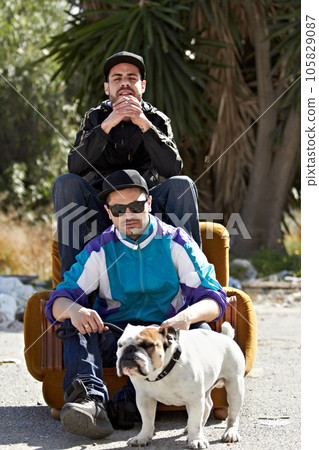Portrait, retro style and dog with friends and their pet outdoor in a downtown neighborhood together. Street, fashion and culture with men and their bulldog puppy on an urban background 105829087