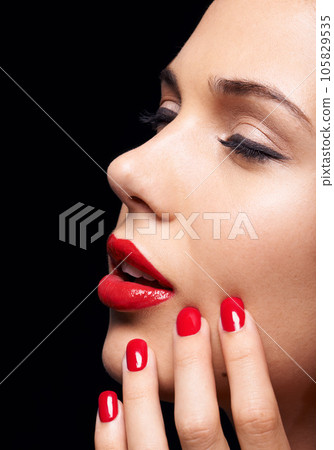 Manicure, makeup and woman with red lipstick and nails in a studio with a self care pamper treatment. Cosmetic, beauty and closeup zoom of a female model with a facial routine by a black background. Manicure, makeup and woman with red lipstick and nails in a studio with a self care pamper treatment. Cosmetic, beauty and closeup zoom of a female model with a facial routine by a black background. 105829535