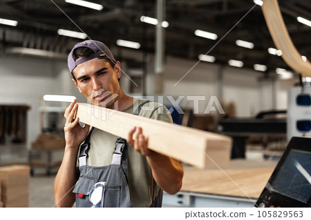 Young carpenter man looking and choosing wood plank at workshop in carpenter wood factory 105829563