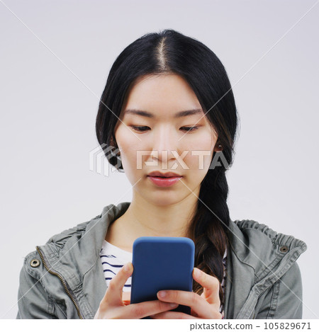 Phone, online and face of Asian woman in studio for social media, internet and typing message. Communication, white background and Korean female person on smartphone for website, mobile app and text 105829671